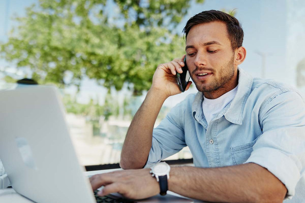 Junger Mann arbeitet draußen an einem Laptop und telefoniert, symbolisiert mobiles Arbeiten und flexible Arbeitsmodelle wie Homeoffice
