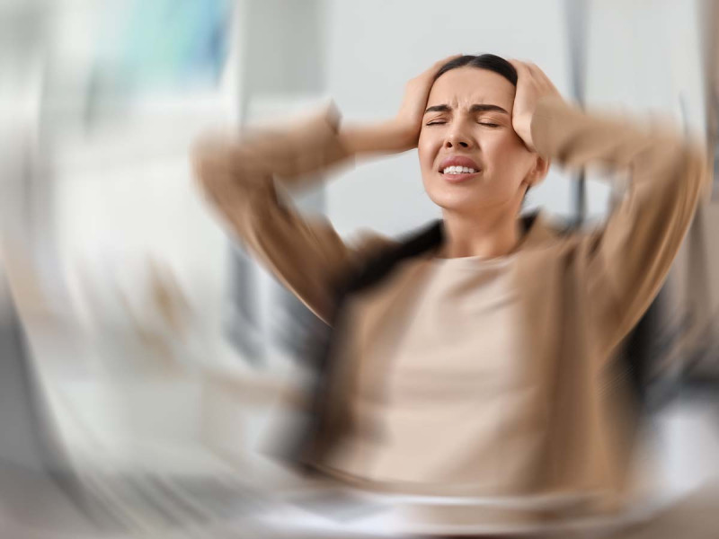 Frau mit Kopfschmerzen hält sich den Kopf, unscharfer Hintergrund, symbolisiert Stress und Druck durch den Arbeitgeber bei Krankheit.