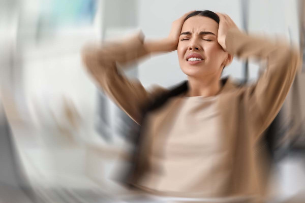 Frau mit Kopfschmerzen hält sich den Kopf, unscharfer Hintergrund, symbolisiert Stress und Druck durch den Arbeitgeber bei Krankheit.