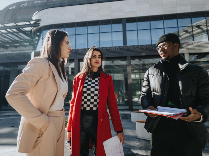 Ein multikulturelles Business-Team, gekleidet in stilvolle Wintermäntel, vertieft sich ernsthaft in eine Diskussion im Freien. Mit Unterlagen in der Hand strahlen sie Professionalität aus.