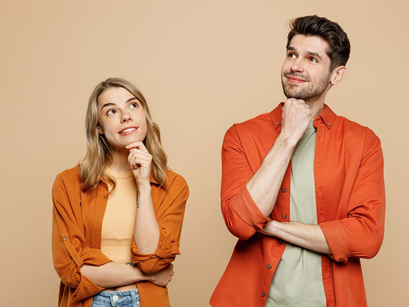 zwei Freunde – Mann und Frau – in lässiger Kleidung, die Hand an das Kinn gelegt, vertieft in Gedanken und Überlegungen, gemeinsam auf hellem, pastellfarbenem, beigefarbenem Studiohintergrund überlegen, ob ein Arbeitgeber eine SCHUFA-Auskunft verlangen darf.