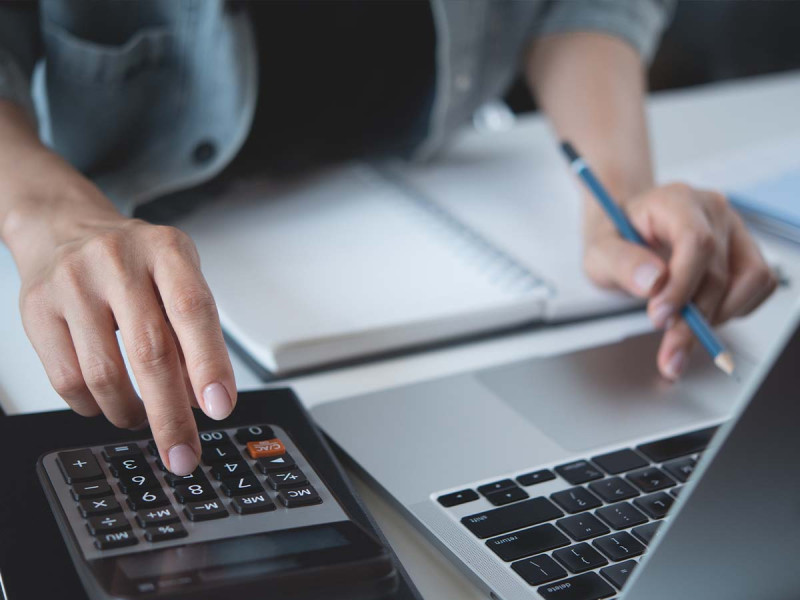 Person berechnet Steuern und Buchhaltung am Laptop mit Taschenrechner, erstellt Lohnabrechnung für nebenberuflich selbstständige Kleinunternehmer und Freelancer.