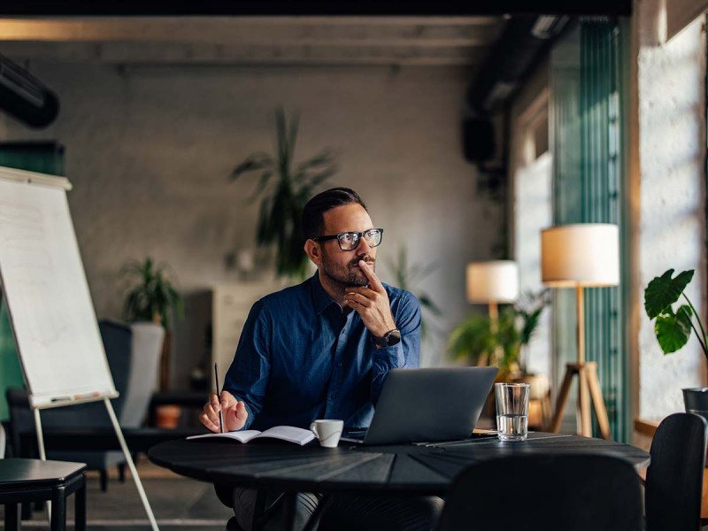 Mann im modernen Büro plant, sich nebenberuflich selbstständig zu machen, prüft Steuern und Buchhaltung für Kleinunternehmer, um als Angestellter nebenbei selbstständig zu sein