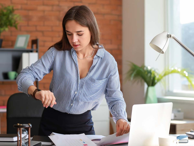 Wöchentliche Arbeitszeit: Frau blickt auf die Uhr, um zu überprüfen, ob ihr Feierabend bereits erreicht ist oder ob sie sich noch innerhalb ihrer täglichen Arbeitszeit befindet.