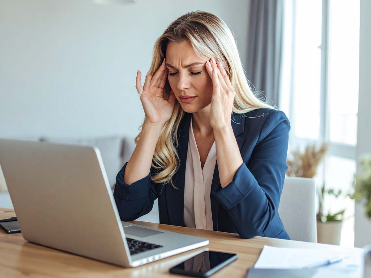 Gestresste Geschäftsfrau mit Kopfschmerzen vor dem Laptop – Risiken von Work-Life-Blending wie ständige Erreichbarkeit und mentale Überlastung im Homeoffice-Alltag.