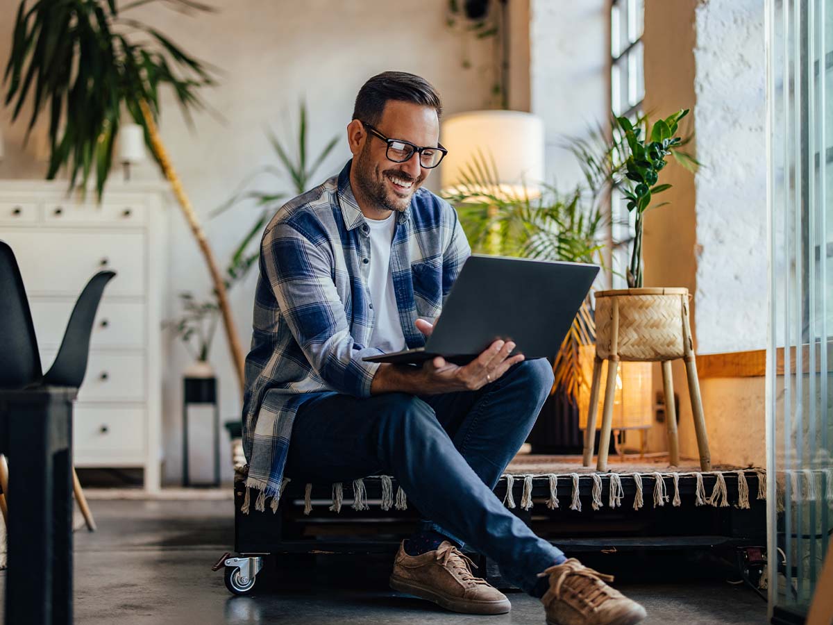 Glücklicher Mann arbeitet nebenberuflich selbstständig im Homeoffice, verwaltet Buchhaltung und Steuern als Kleinunternehmer, während er hauptberuflich angestellt ist.