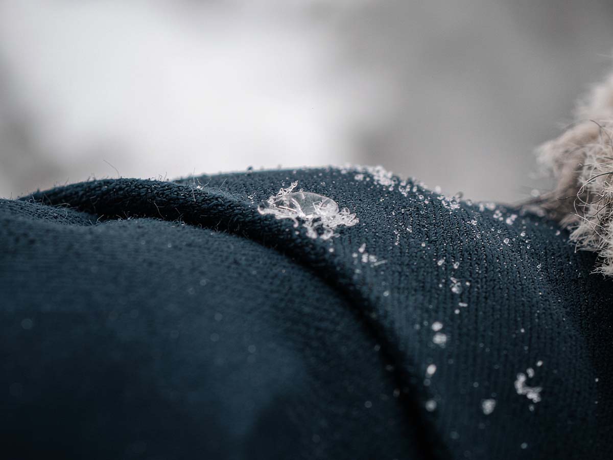 Makroaufnahme eines metallischen Reißverschlusses an einer dunklen Winterjacke mit braunen Stoffnähten. Die Detailaufnahme zeigt die hochwertige Verarbeitung und symbolisiert Schutz, Funktionalität und Strapazierfähigkeit bei winterfester Kleidung.